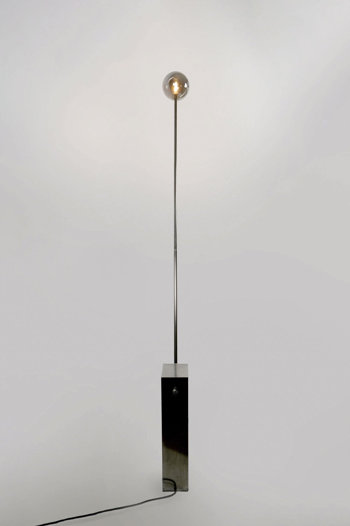 Modern floor lamp with sleek black marble base and thin metal rod supporting smoky glass globe bulb