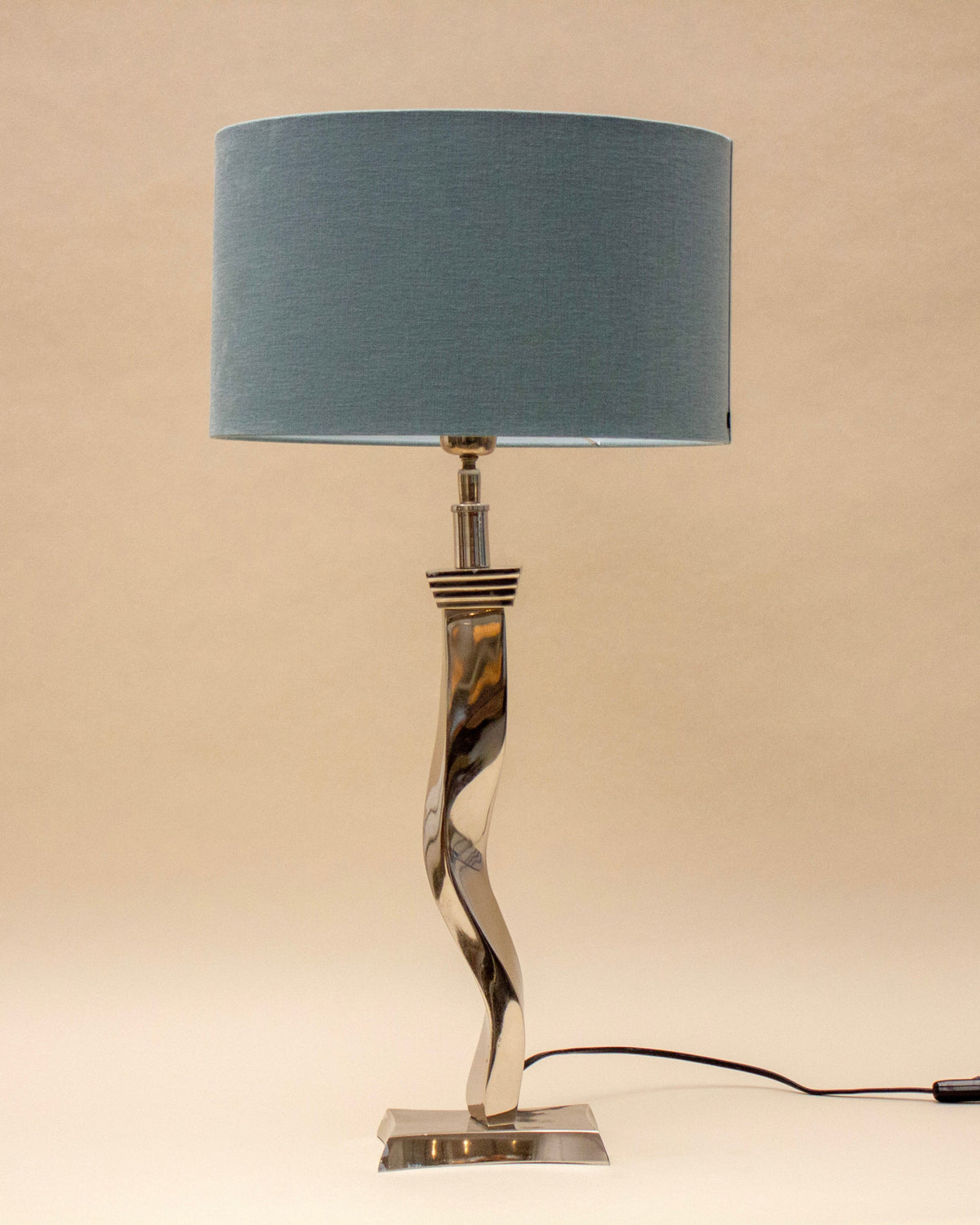 The SÒLER TAVIRA BLUE LAMP features a twisted metal base, a large sky blue lampshade, and a black power cord, perfect for adding modern style to any flat surface.