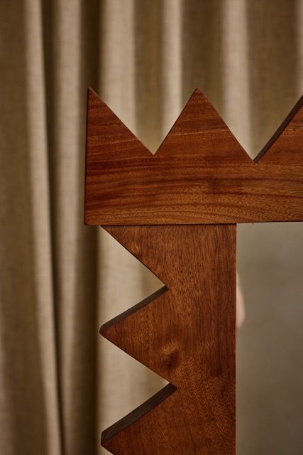 Close-up of the Jura Mirror by Ah Um Design Studio, featuring a solid mahogany frame with jagged, crown-like zigzag edges, set before beige curtains—a bold statement piece with strong geometric lines.