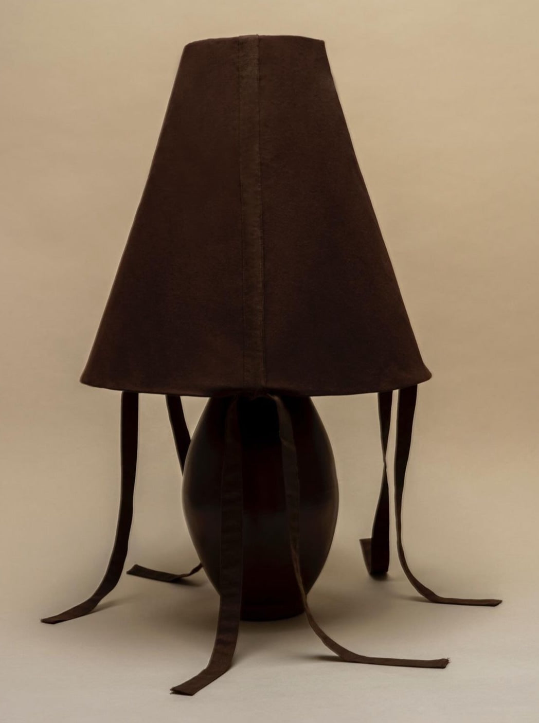 Brown ceramic table lamp with sculptural leather strap legs and dark linen shade