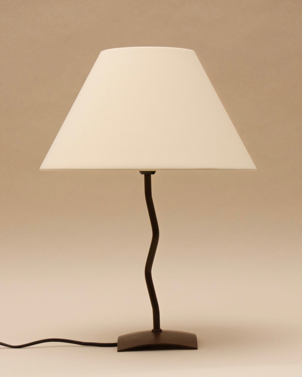 The SÒLER BILBAO TABLE LAMP features a black metal base, twisted stand, and vintage white shade. It sits on a flat surface with its cord visible, set against a plain beige background.