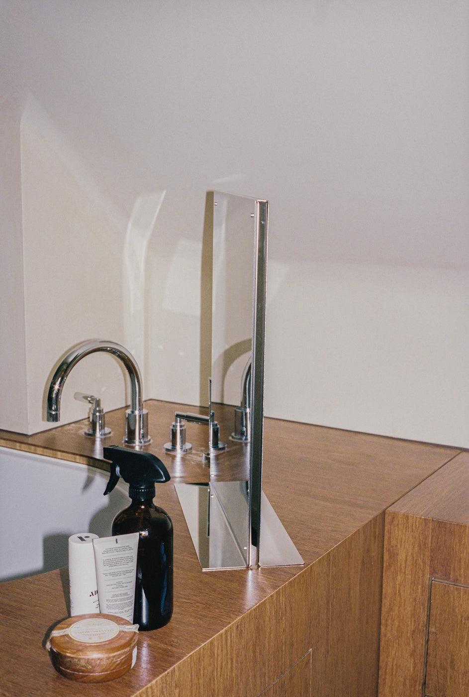 Flat mirror on wooden vanity with chrome faucet and toiletries