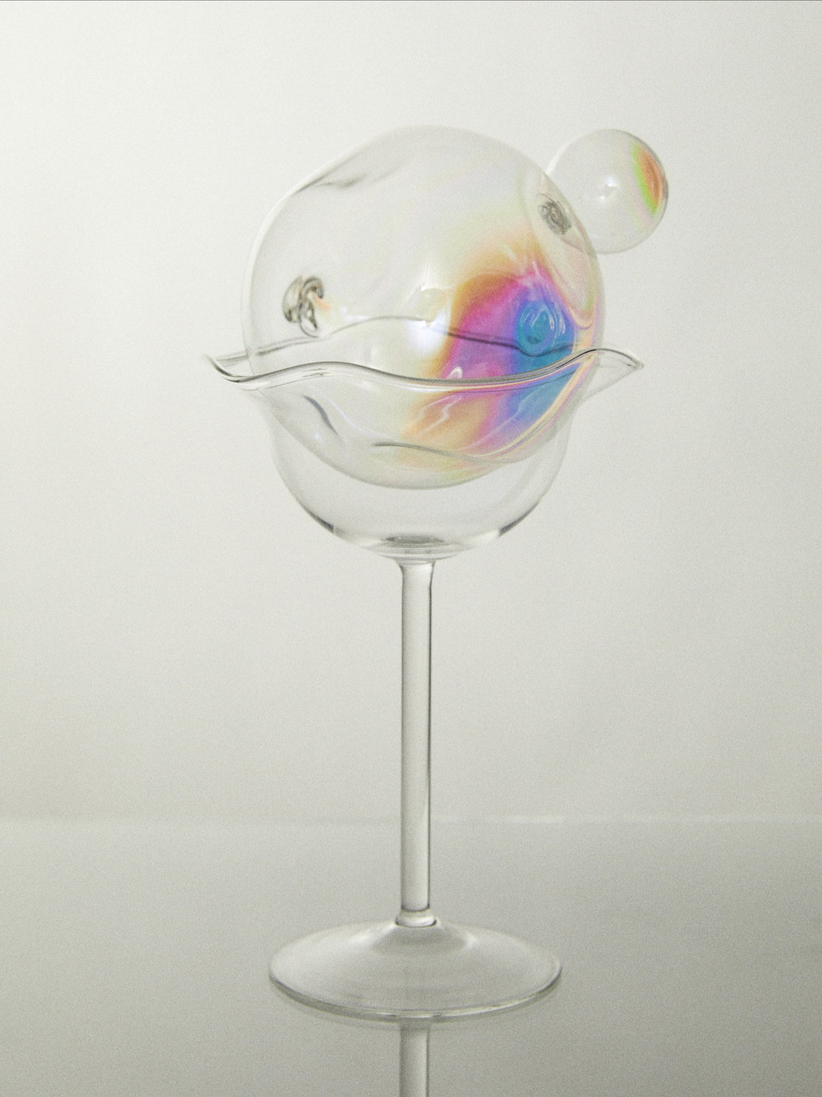 Iridescent soap bubble floating above clear wine glass on stem