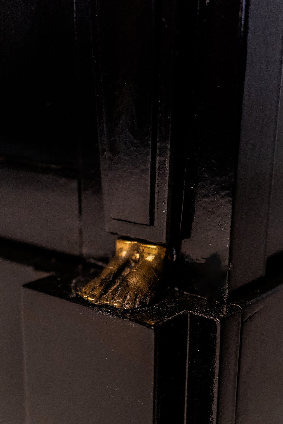 A close-up of Barracuda Interiors' 'Return of Egypt' Lacquered Drawers, 19th c, showcasing a glossy black finish and a small gold sculpted foot set at the corner for striking contrast.