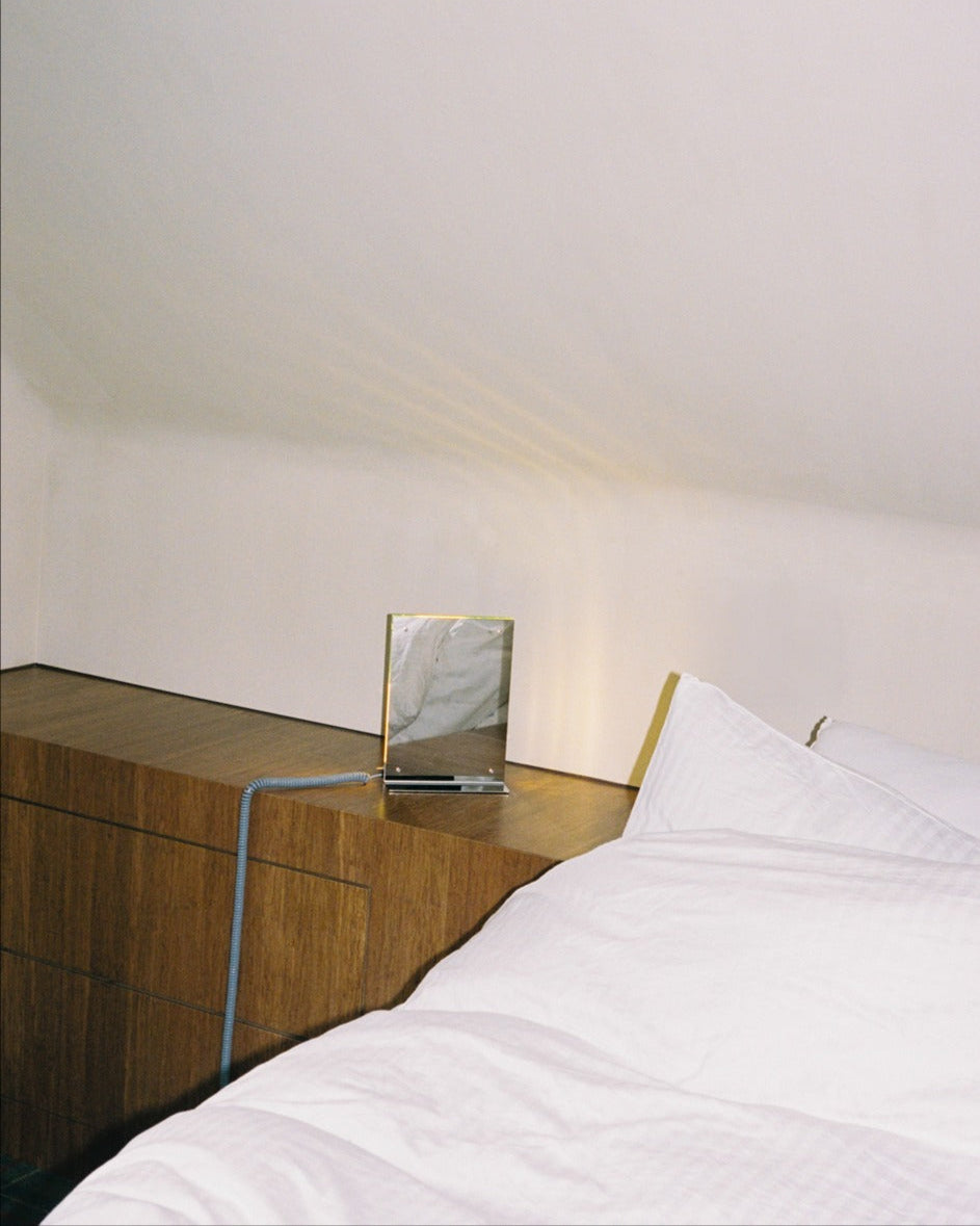 Flat Light table lamp on walnut nightstand beside white bedding