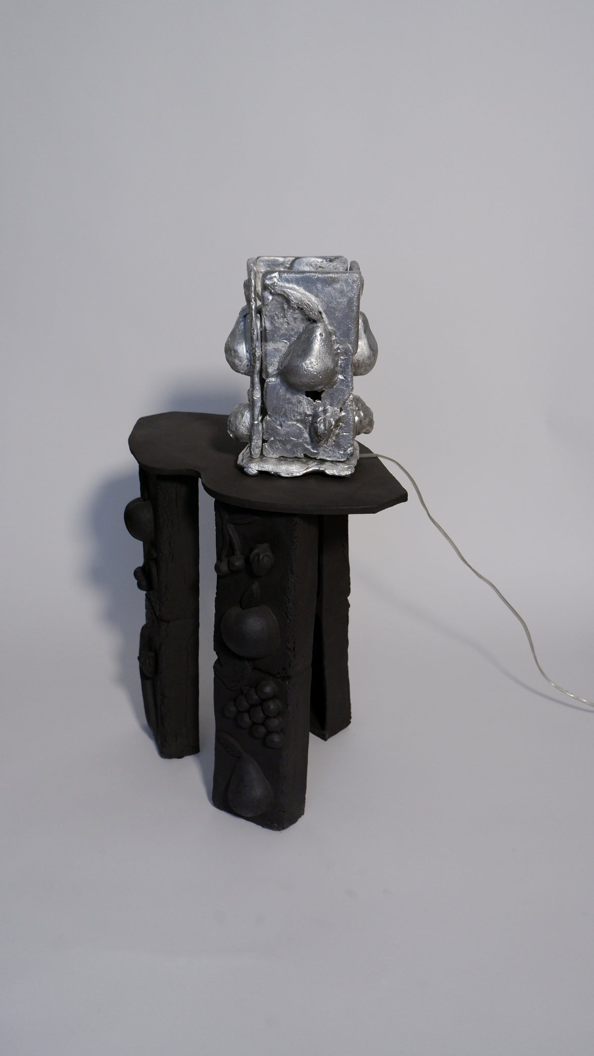 Tender table lamp with sculptural metallic form on black carved base