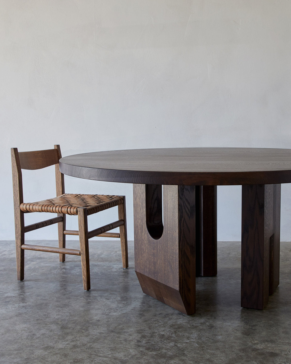 Tulia Round Dining Table — side angle showing dark wood and woven chair