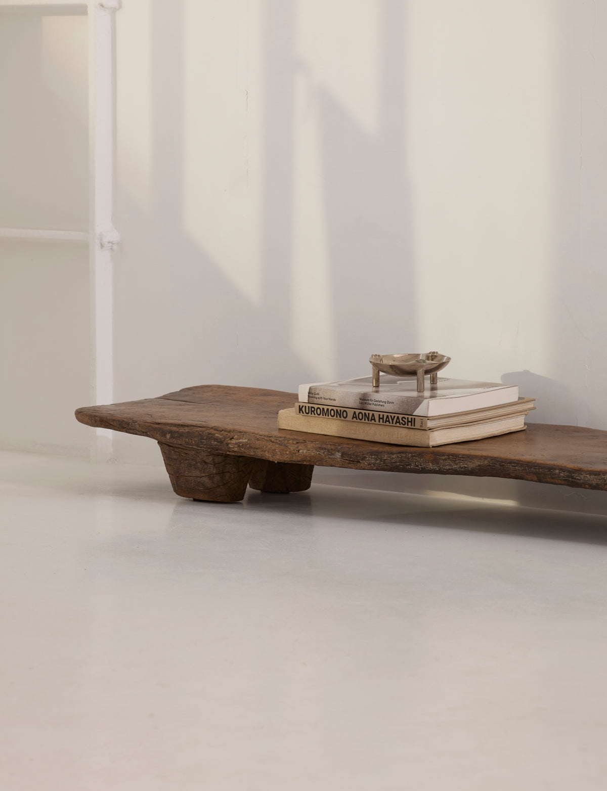Carved Senufo Bench in Wood — side angle with stacked books on top