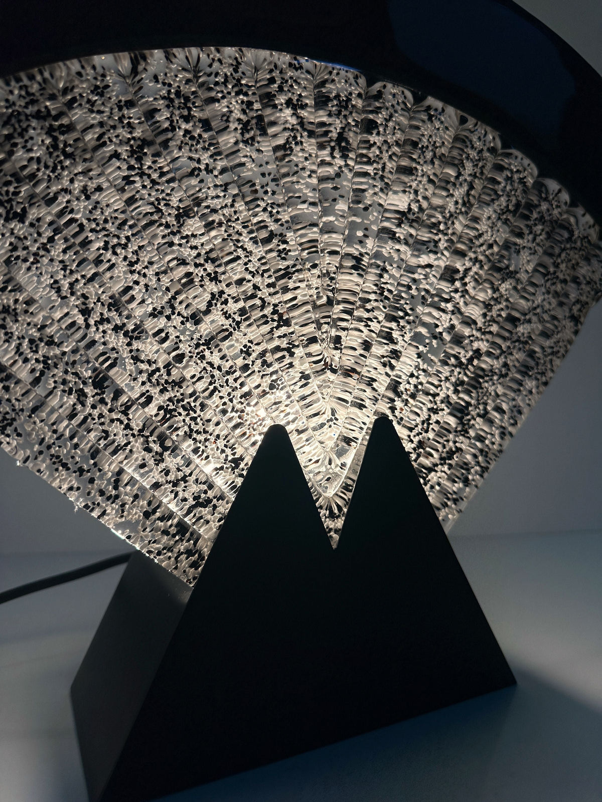 The Large Murano glass fan lamp by Dodo Vintage is an Art Deco piece from the 1980s, featuring a textured acrylic diffuser and a black triangular base, illuminated from below for striking light patterns.