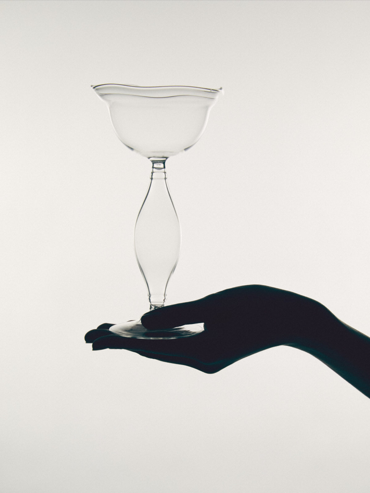 Hand holding clear Crater wine glass with sculptural stem
