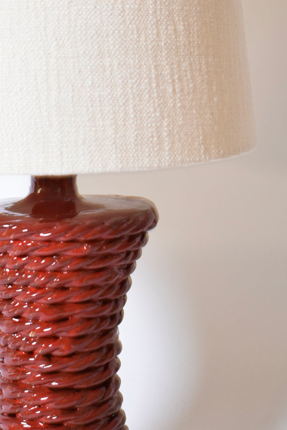 A close-up of the "Kasaï" Red Ceramic Table Lamp by Barracuda Interiors showcases its textured, glossy reddish-brown base and white fabric shade, making it a standout piece for refined interior design.