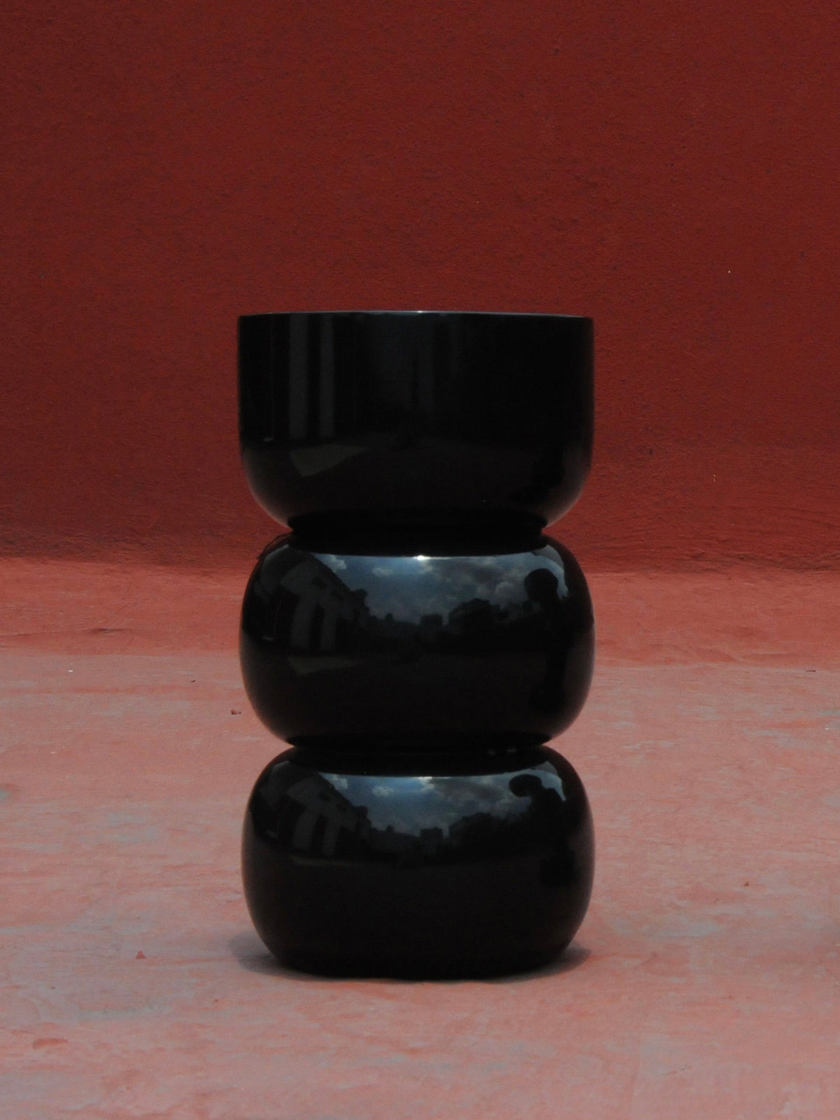 Chess' Stool convex in lacquer wood — front view against red wall