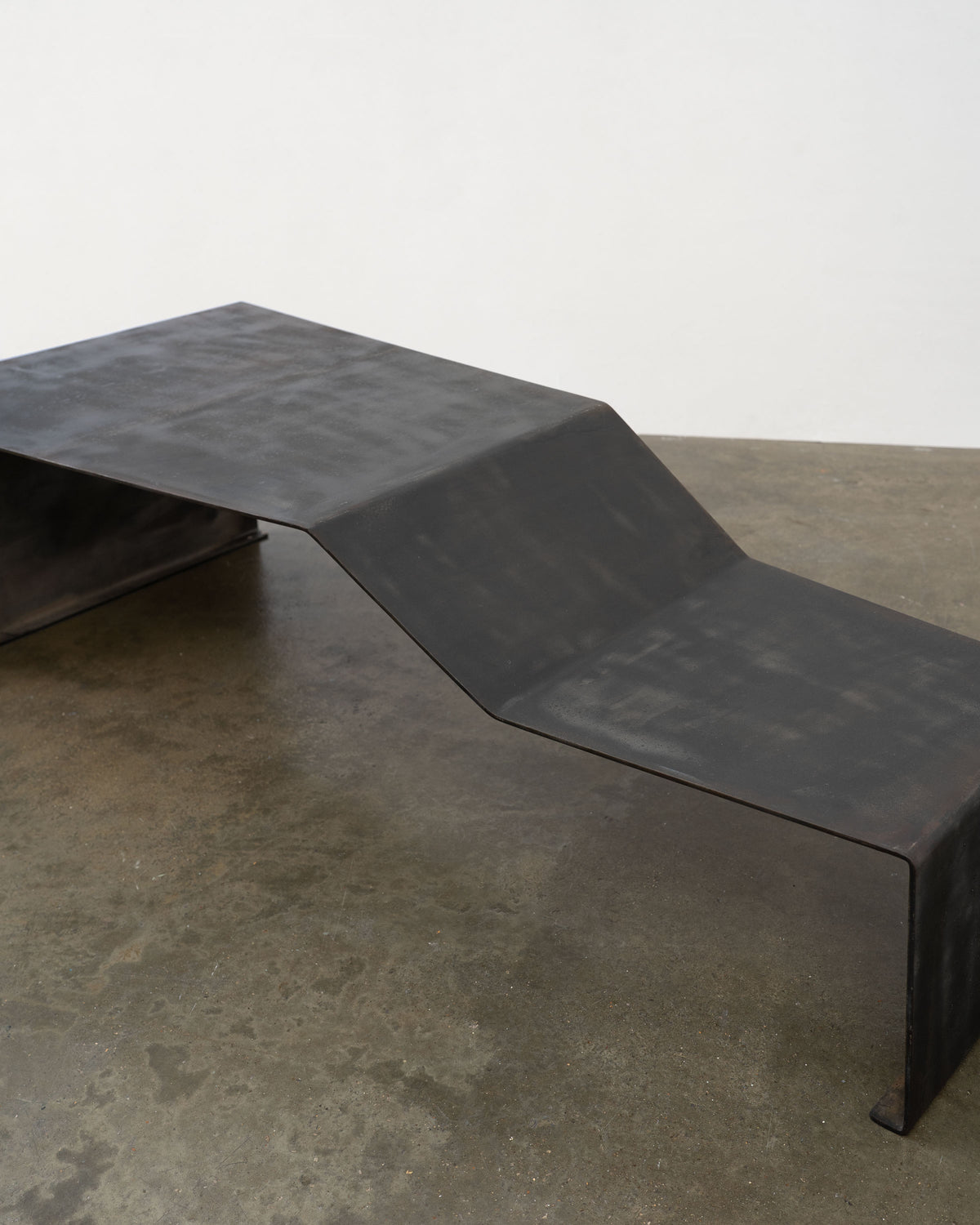 Profile view of patinated steel bench coffee table showing curved form