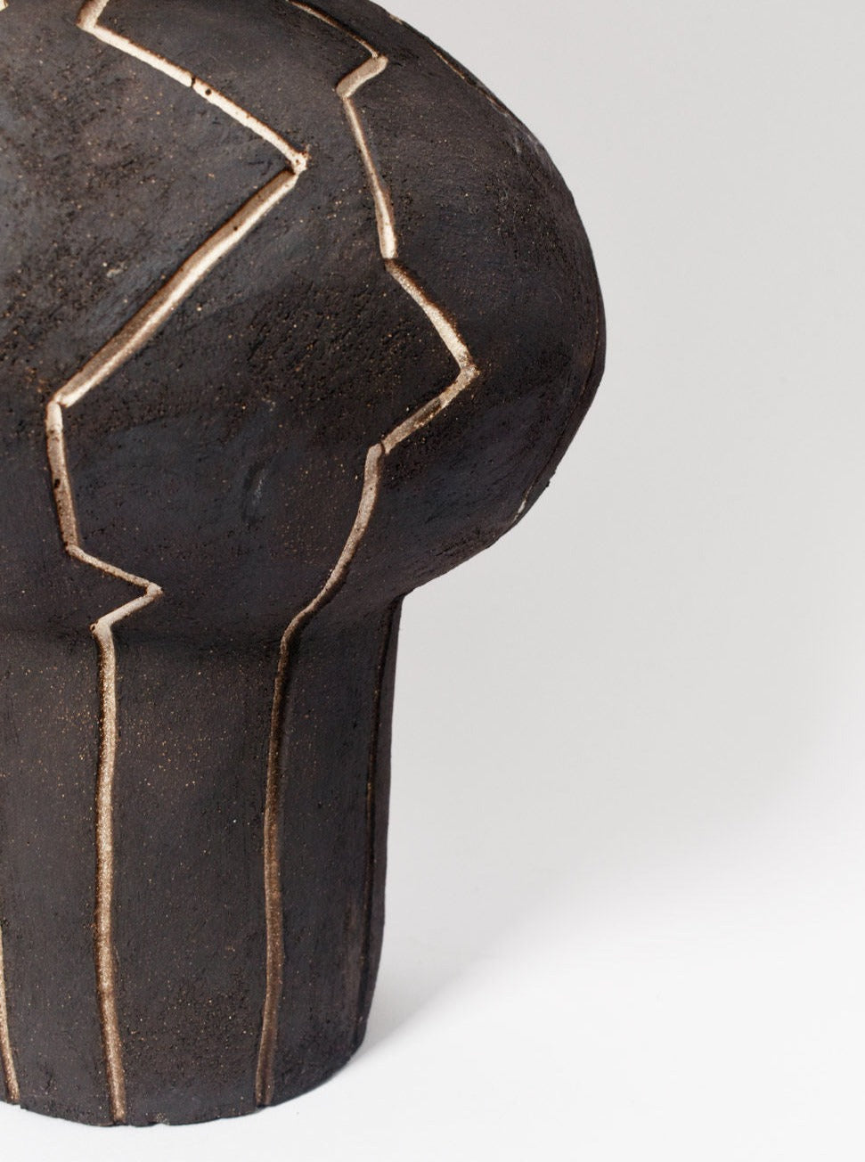 The "Lanzarote" Lamp by Barracuda Interiors features a dark ceramic body with a rounded top and vertical zigzag carvings that reveal a lighter color beneath—a striking piece, ideal for customizable interior lighting.