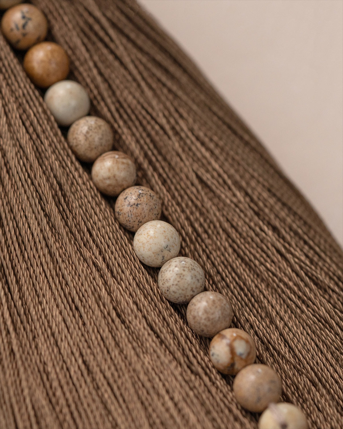 Natural beaded tassel ornament with earth-tone spheres on wood