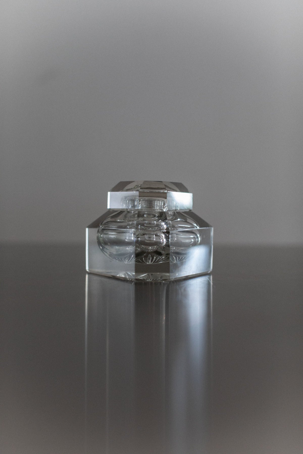 Clear glass perfume bottle with ornate stopper on reflective surface