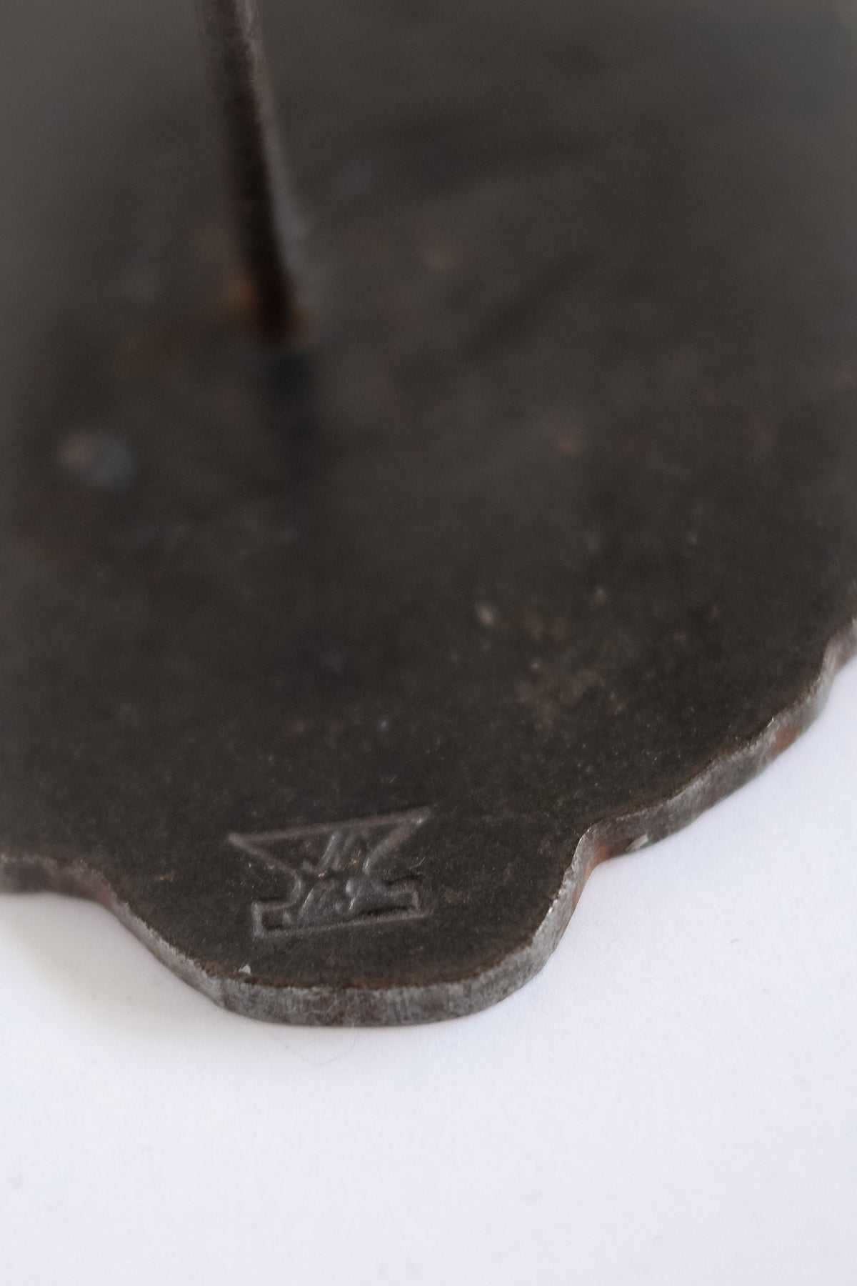 Close-up of a dark, irregular Pieter Spruyt Copper Candle Sconce by septembre studios, featuring a small engraving near the wavy edge. The aged finish and thin rod recall vintage floor candleholder style.