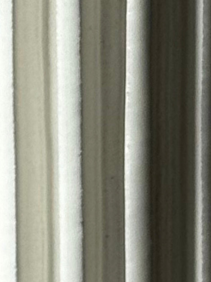Close-up of vertical white and light gray fabric folds creating a soft, textured effect with subtle shadows—echoing the gentle contours found in Devin Wilde’s Vessel No. III.