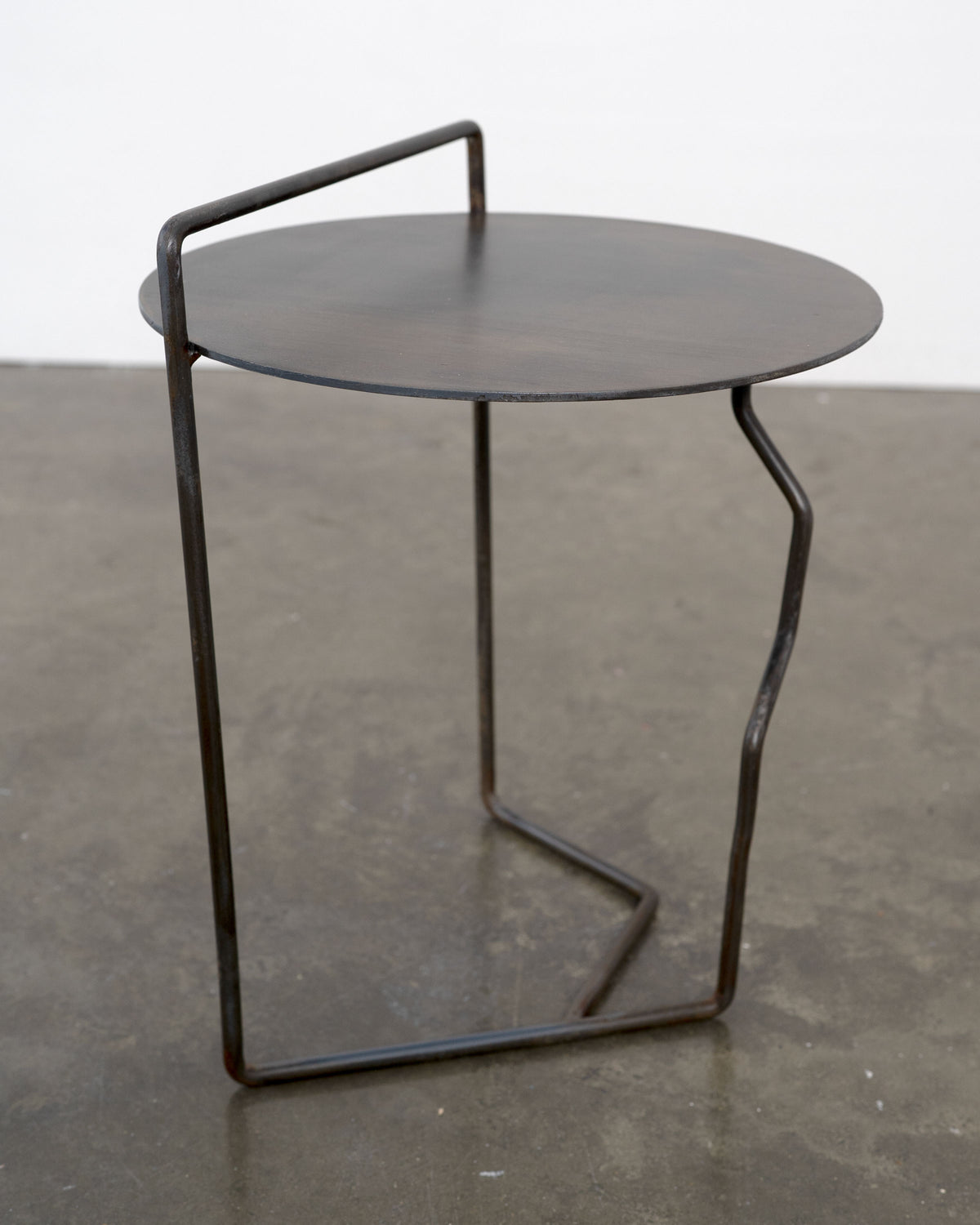 Sculptural Patinated Steel Side Table — angled view on concrete floor
