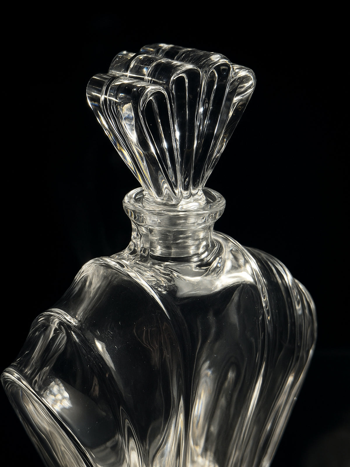 A close-up of the Italian crystal Glass Art Deco Decanter by Dodo Vintage (1980s) shows its elegant, faceted stopper and curves reflecting light against a black backdrop, highlighting its intricate, vintage design.