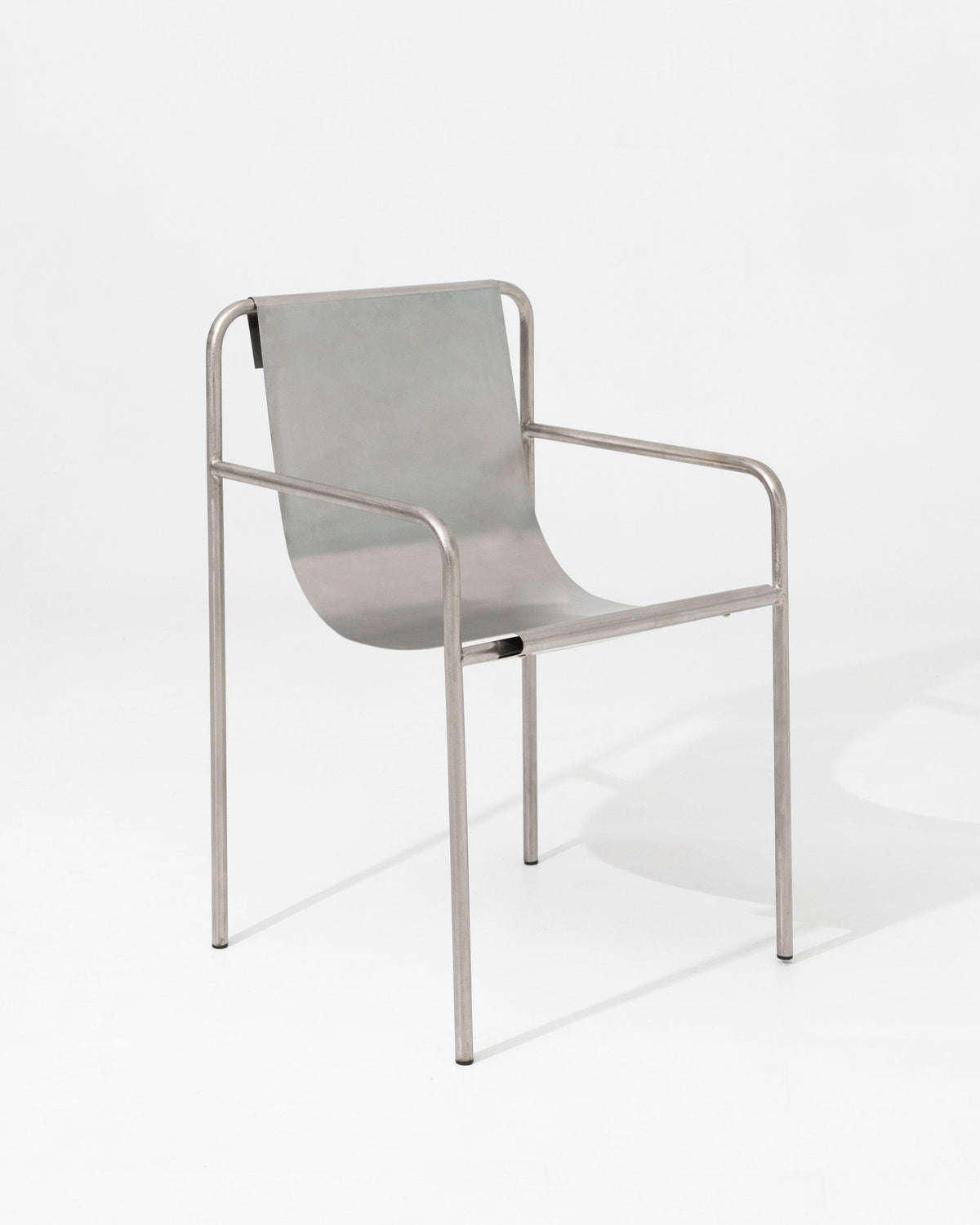 The DESSERT chair by SALAK features a curved seat and backrest with slim tubular armrests and legs, creating a sculptural, minimalistic piece ideal for modern interiors.