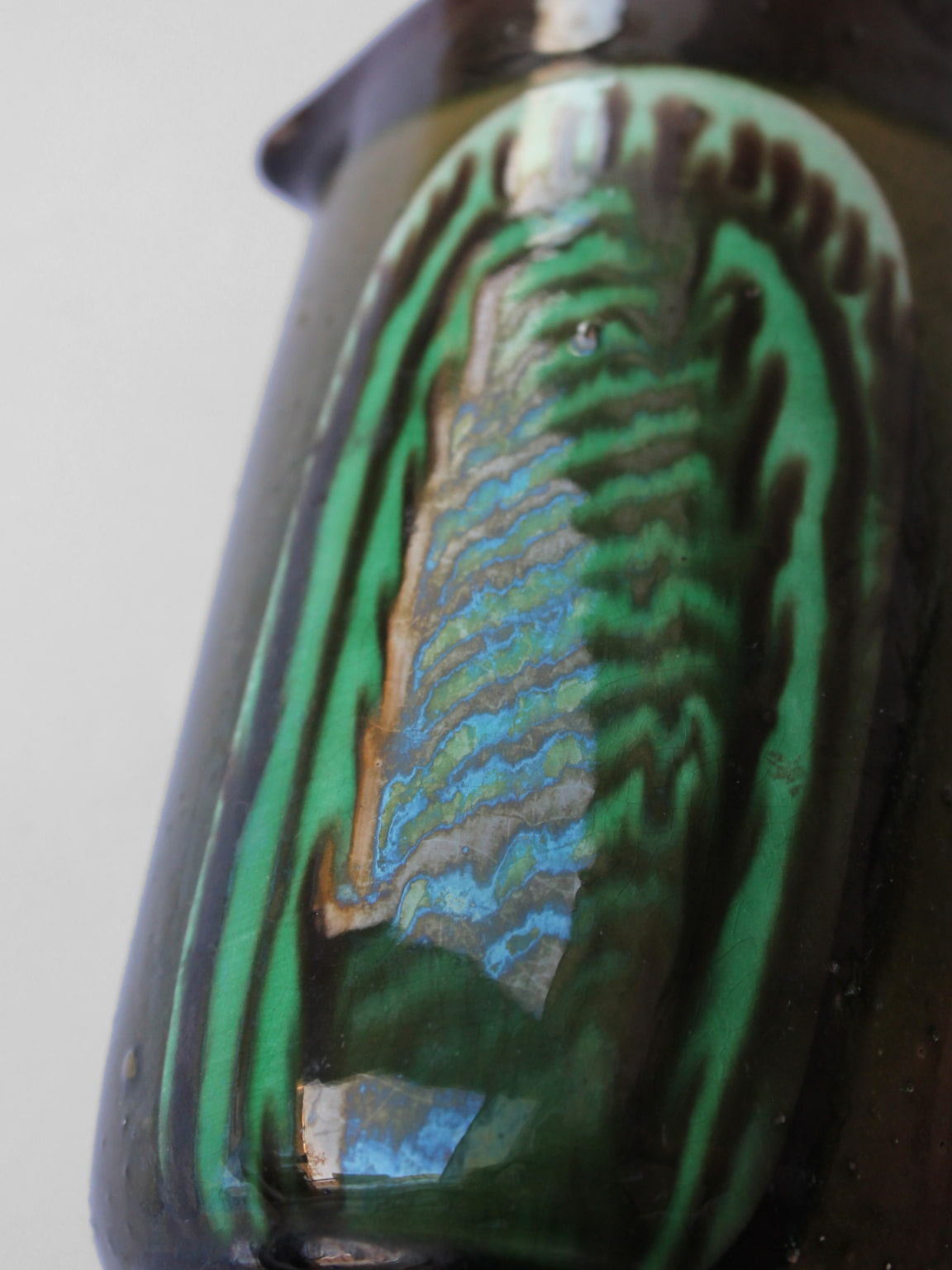 Close-up detail of green glazed ceramic pitcher with iridescent finish