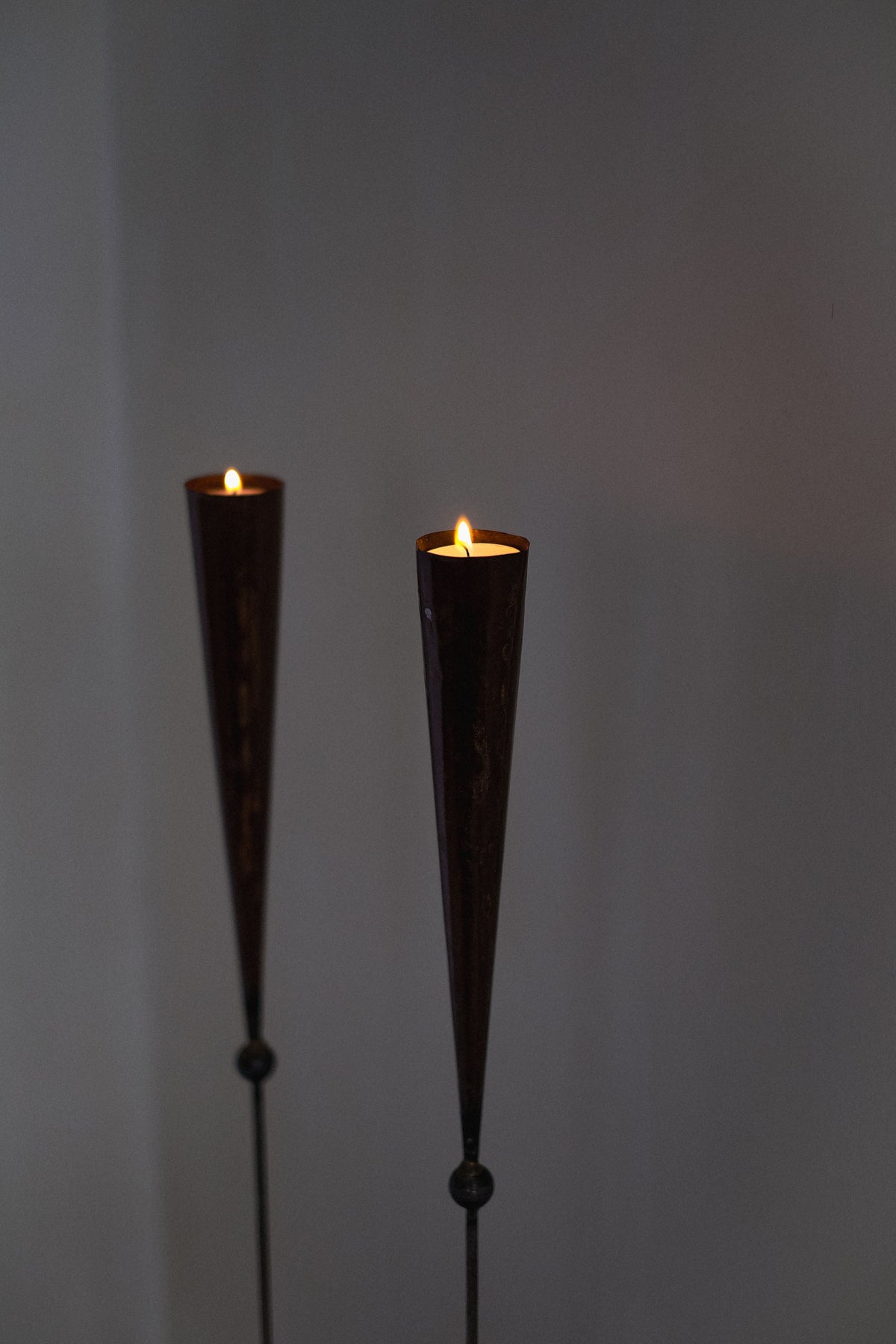 The Pieter Spruyt Copper Candle Scones by septembre studios, two elegant vintage candle holders with lit candles, cast a soft, warm glow against a simple, dimly lit background.