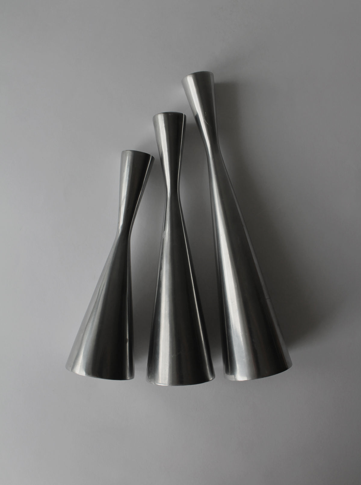 Three polished aluminum candle holders with curved hourglass silhouettes