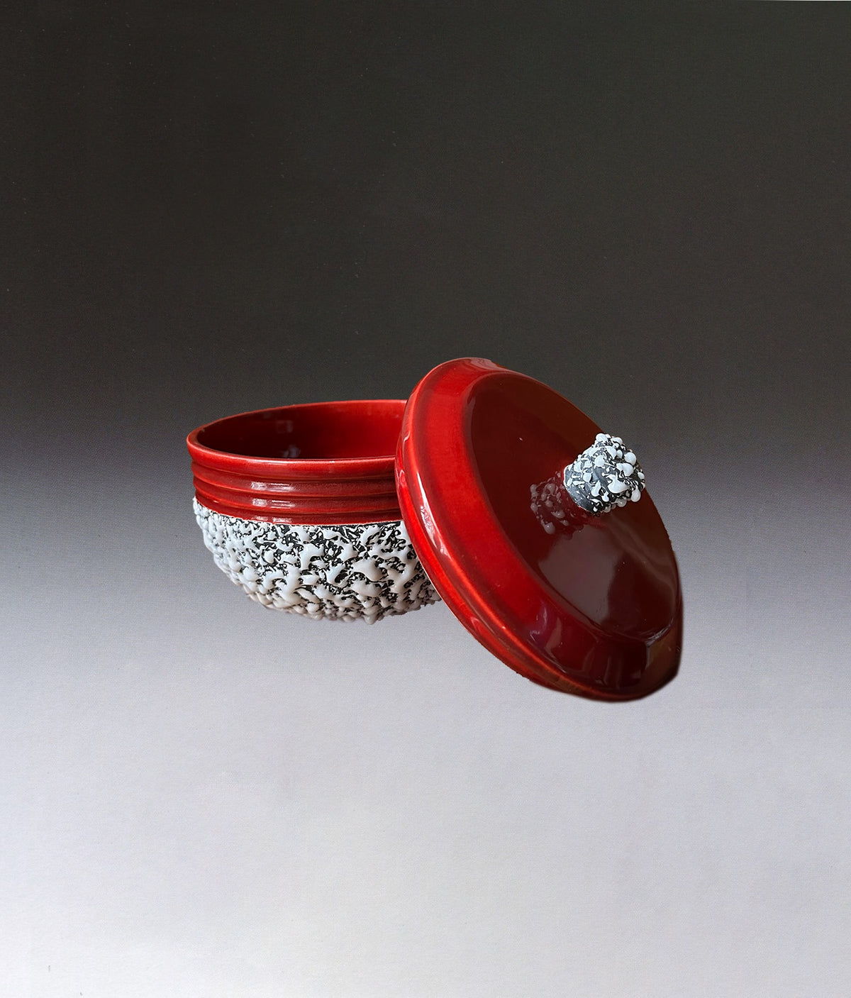 The Art Deco Ceramic Oxblood Box by Paul Millet Manufacture de Sevres, from STUDIO ASAC, features a red lacquered bowl with a white carved base and a matching lid with a white handle, displayed against a smooth gradient background.