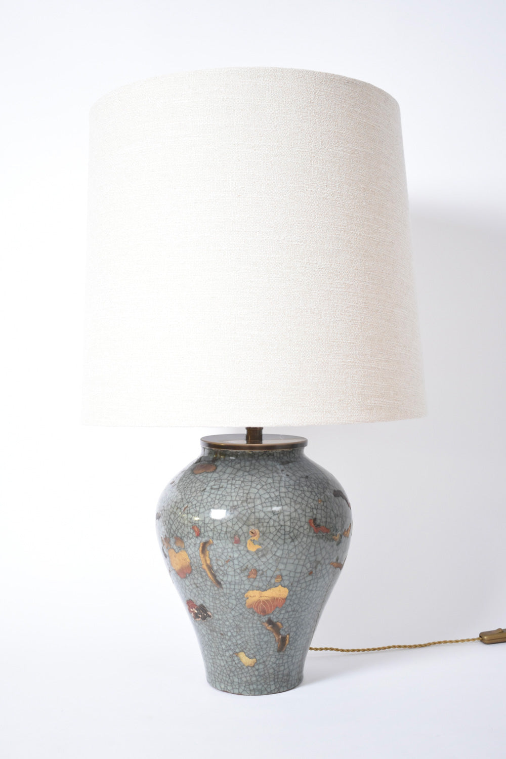 The Chinese Celadon and Gold Lamp by Barracuda Interiors features a textured light grey base with orange and brown floral accents, an off-white fabric shade, and a short gold power cord. Inspired by XIXth c. Chinese design.