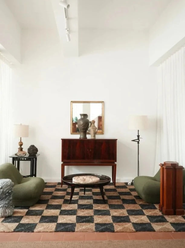 A modern living room with a checkered rug, two green floor chairs, a round coffee table, a wooden cabinet with a mirror above, and Brejos Floor Lamps from Barracuda Interiors for customizable lighting, plus minimal décor on side tables.