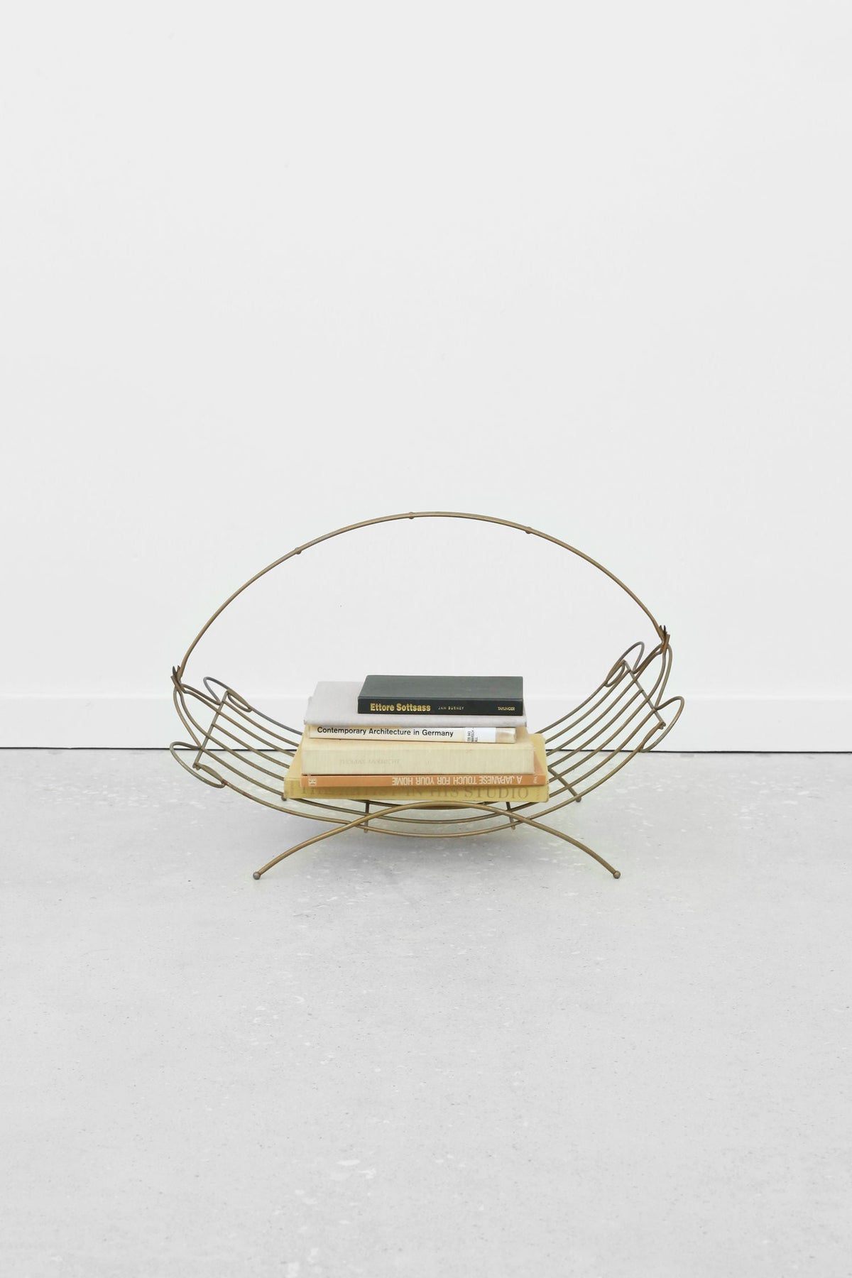 Gold wire magazine rack with books on white floor
