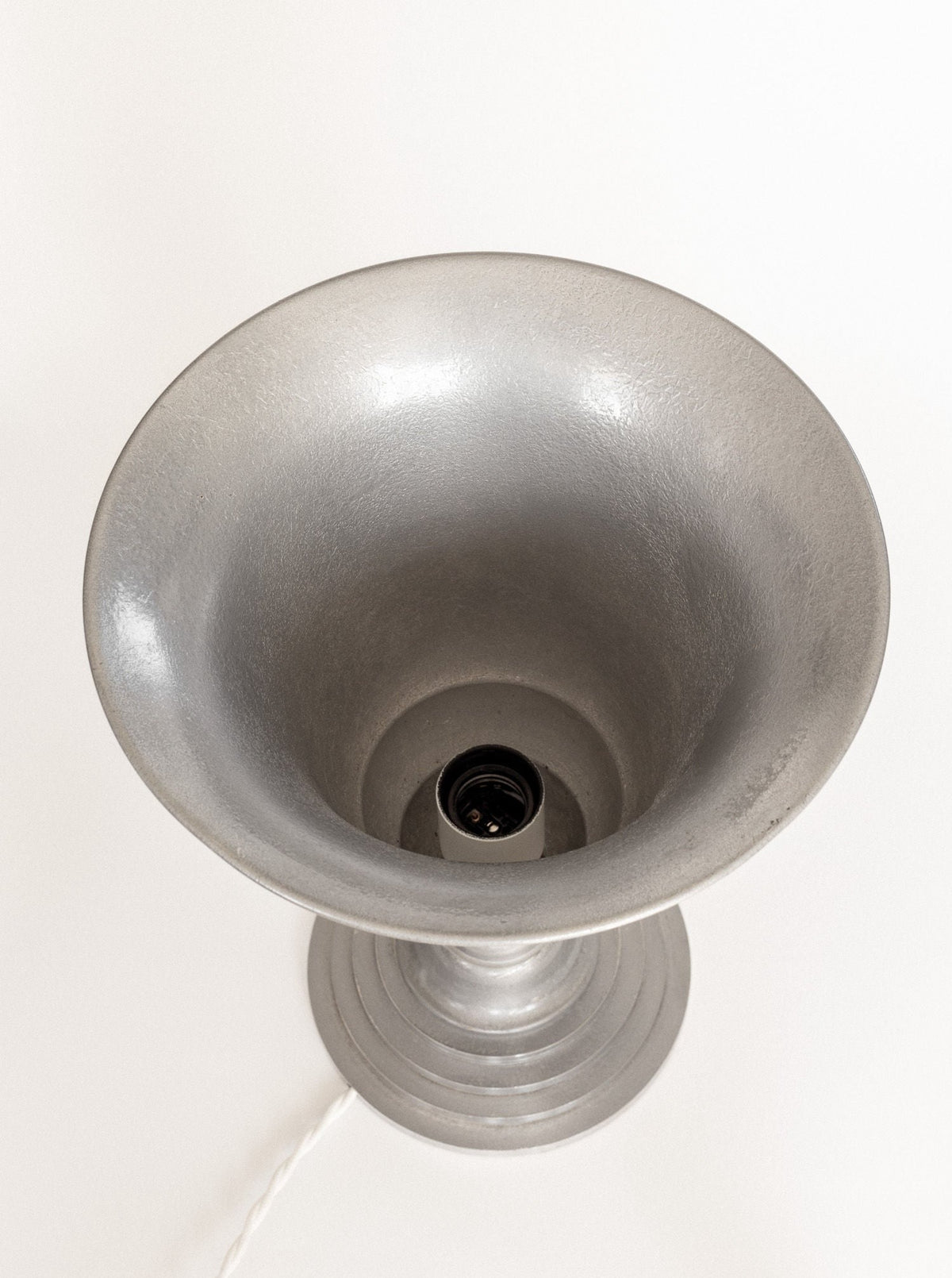 A top view of the Spigel Art Deco Torchière Table Lamp from France, showcasing its oxidized aluminum body without a light bulb. This art deco lamp features a bowl-shaped shade and is attached to a visible white power cord extending from the base. The surface exhibits a textured, matte finish.