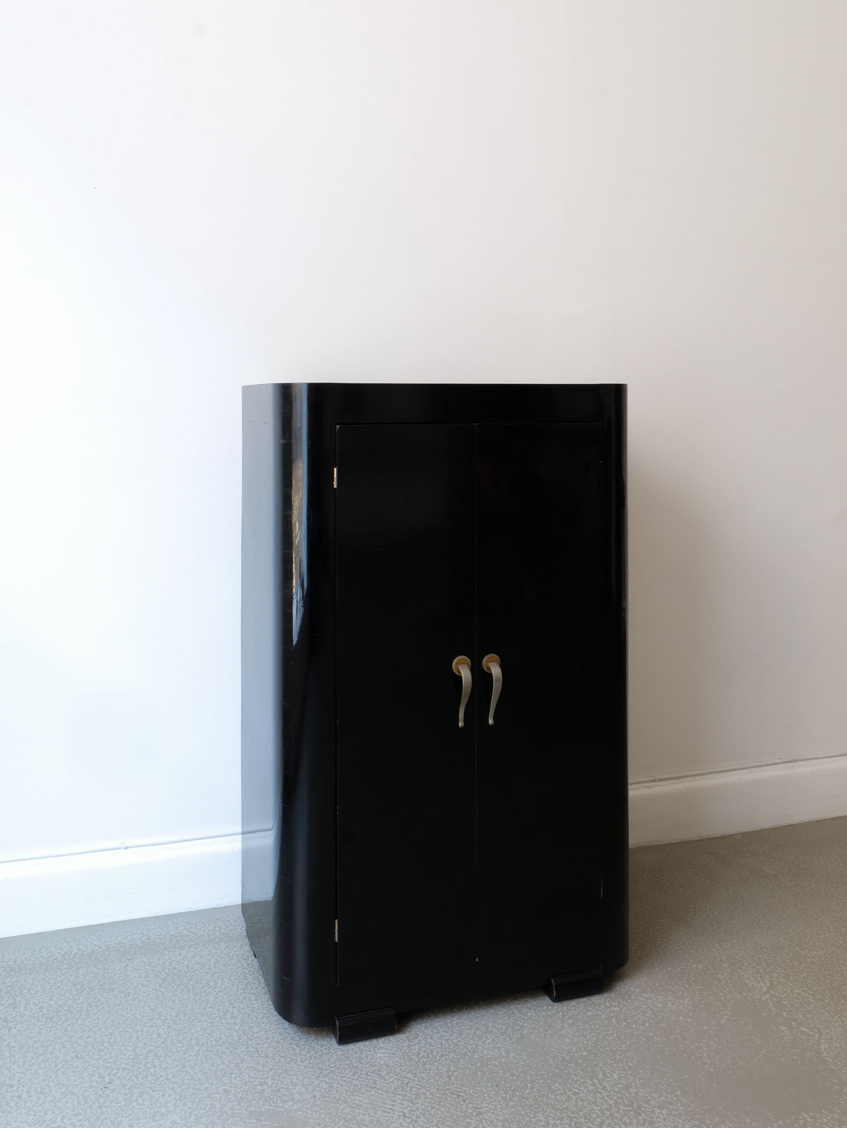 The French Deco Cabinet 1930s by Collection apart stands on a gray floor against a plain white wall. This vintage Art Deco piece features two doors with curved silver handles and a sleek, glossy finish.