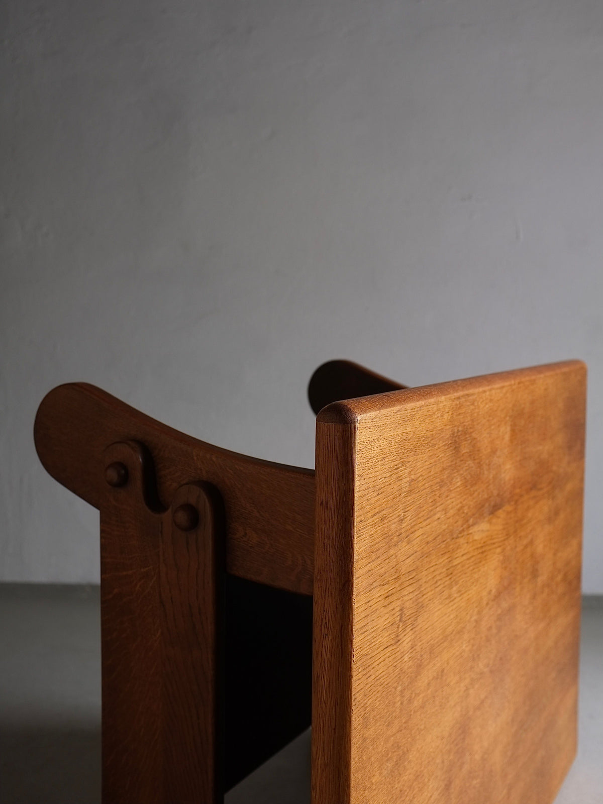 A Brutalist Oak Coffee Table | Netherlands | 1970s by Veter Vintage is positioned against a plain gray wall. The table features a straight backrest and subtly curved armrests, reminiscent of 1970s design, showcasing a light brown finish and visible wood grain that highlights its craftsmanship and natural texture.