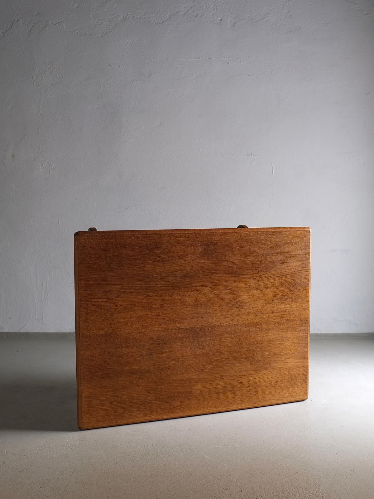A Veter Vintage Brutalist Oak Coffee Table | Netherlands | 1970s stands vertically on a gray concrete floor with a plain, light gray wall in the background. The table's rectangular surface is smooth and has a rich, natural wood grain finish, embodying the 1970s design aesthetic.