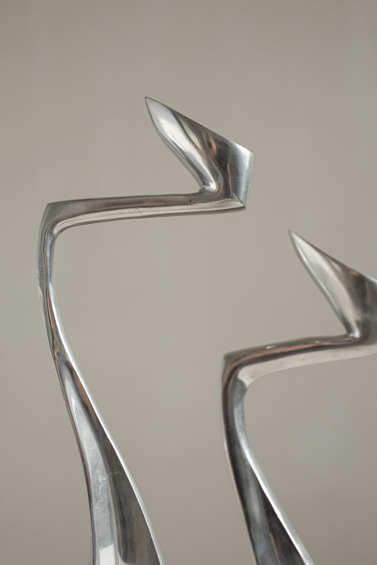 Two abstract silver candleholders by Matthew Hilton from the 80s, available via septembre studios, feature elongated, curved shapes that evoke modern art. Their polished metal surfaces reflect light beautifully against a neutral background, making them ideal collector's pieces for design enthusiasts.