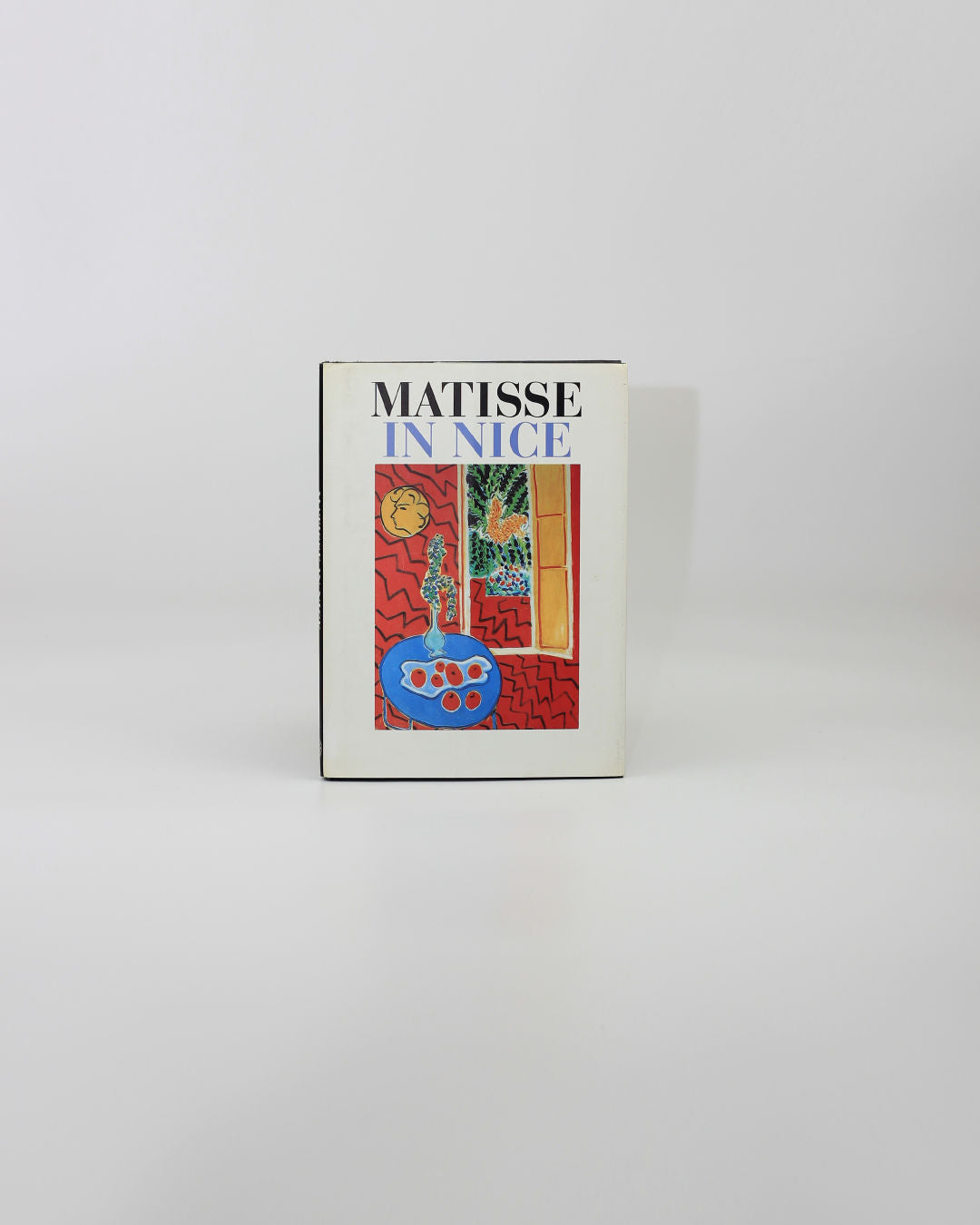 The 'Matisse in Nice' Book from Boga Avante Shop features a vivid Henri Matisse cover with a blue fruit bowl, window, plants, and yellow clock against a bright red background inspired by the South of France.
