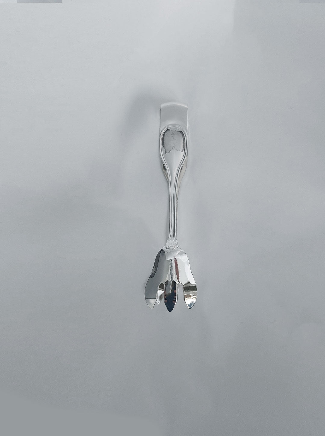 A **Les Objoies Large Sugar Bowl** hangs vertically against a light grey background. The bowl has a smooth handle and scallop-shaped ends, perfect for storing sugar or other condiments, creating a refined tableau.