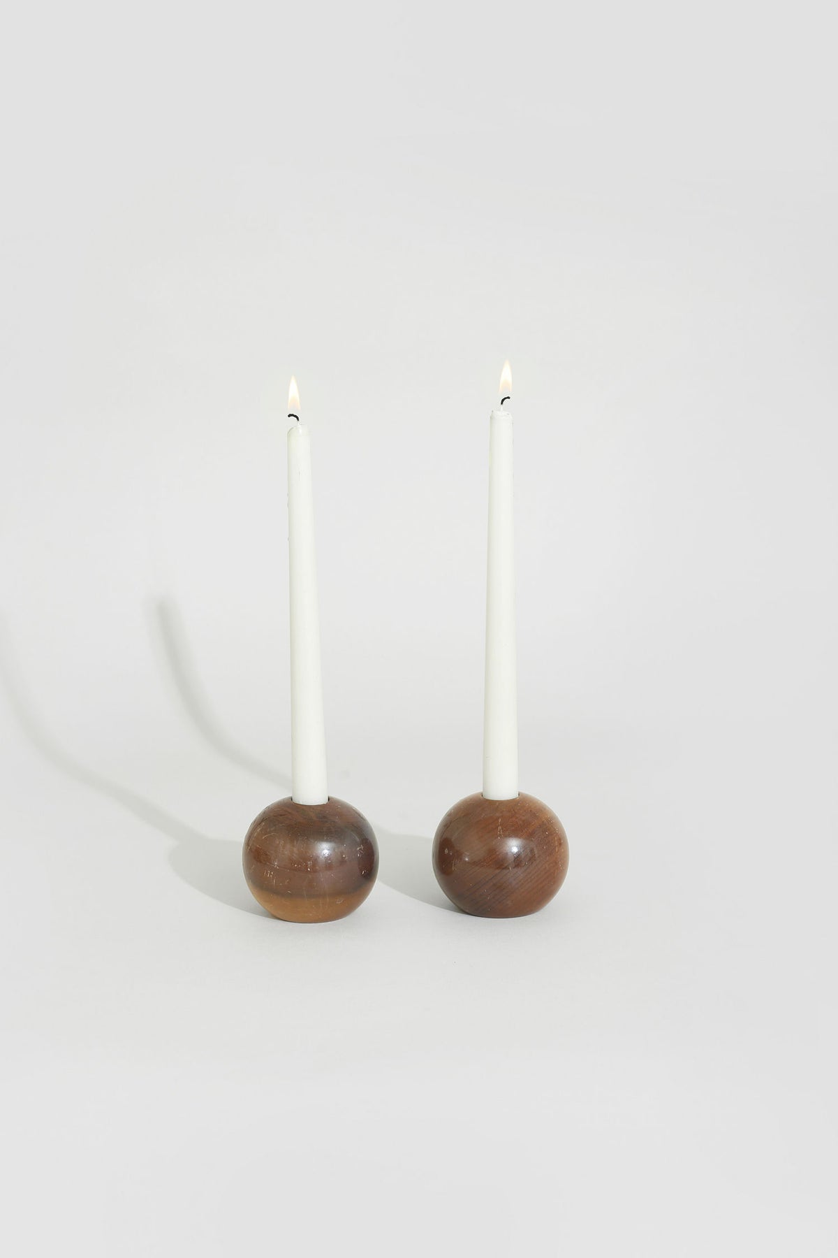 Two lit white taper candles in spherical walnut wood holders