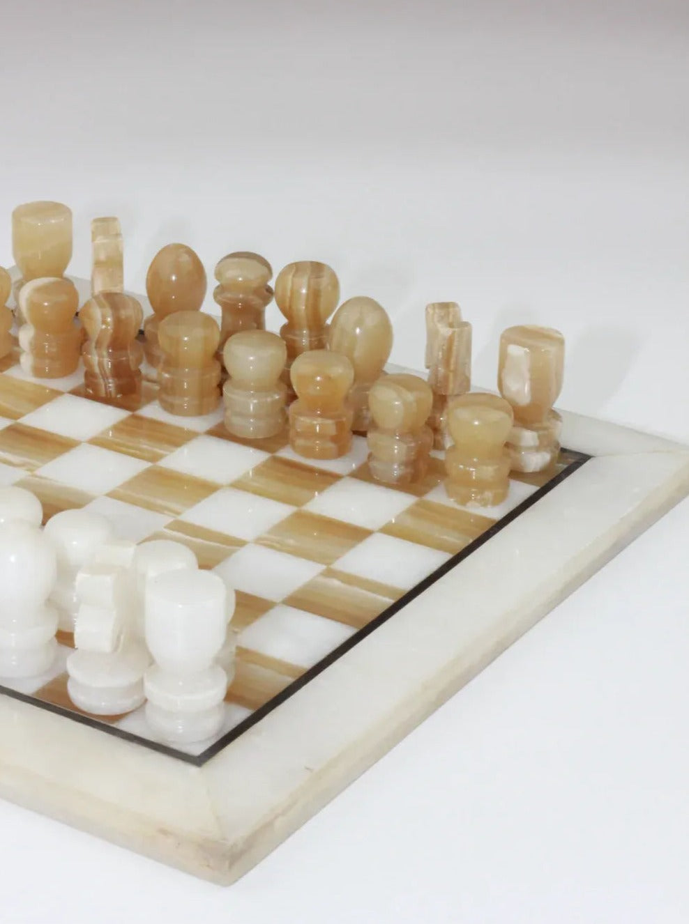 A close-up of a Vintage Marble Chessboard from Boga Avante Shop. The board features alternating white and tan squares, and the hand-carved pieces are in matching colors; the white pieces are at the bottom left, and the tan pieces are at the top right. The pieces are uniquely designed with a smooth finish.
