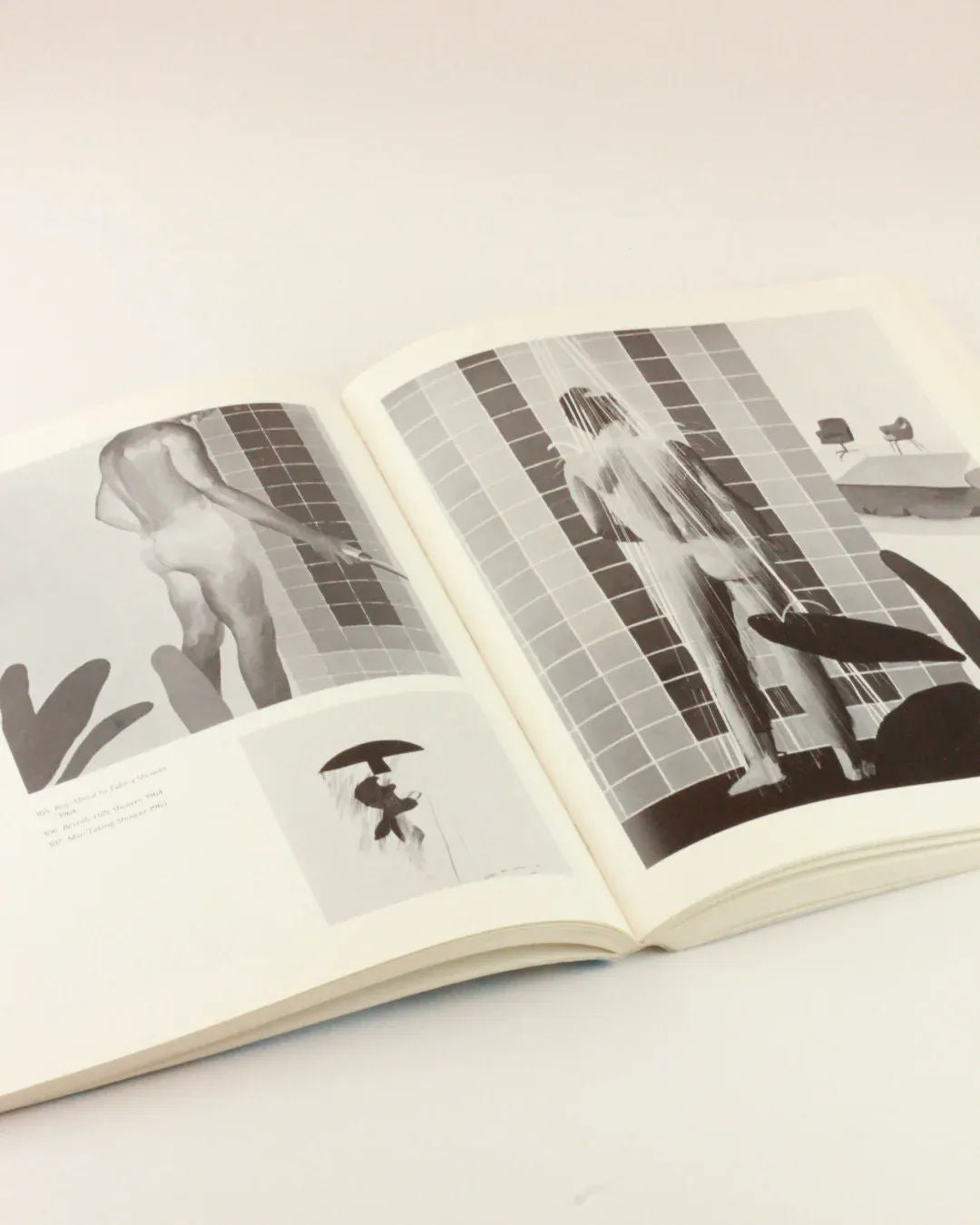 An open David Hockney 'My Early Years' from Boga Avante Shop displayed on a surface, showing black-and-white photographs of a person showering. The imagery captures various angles and views from behind, with tiled walls and shower fixtures visible. The book is propped open, revealing both pages in a style reminiscent of David Hockney's work.