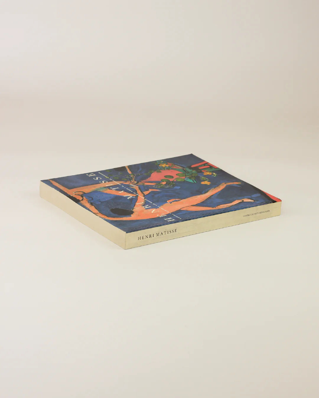 A square book titled "Henri Matisse" from Boga Avante Shop lies on a light surface. Its cover showcases a vibrant Fauvism painting with blue, orange, and green hues, depicting abstract shapes and forms.