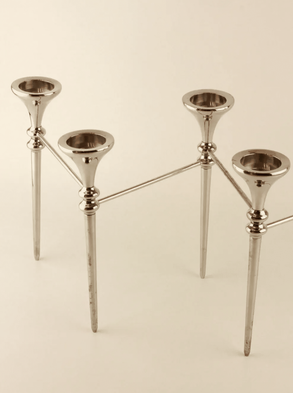 A silver Scandinavian Modular Candelabra by Boga Avante Shop with four evenly spaced candle slots arranged in a linear design. Reminiscent of a vintage chrome chandelier, the sleek, polished metal features a modern and minimalist aesthetic, each slot elevated on a tapered, vertical stand. The background is plain and light-colored.