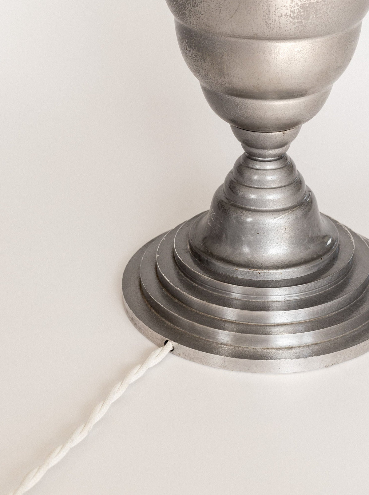Close-up image of the base of the Spigel Art Deco Torchière Table Lamp, France, crafted from oxidized aluminium with a ribbed design resembling a pedestal. A white, twisted cord extends from the base, suggesting it may be an electric device against a neutral background.