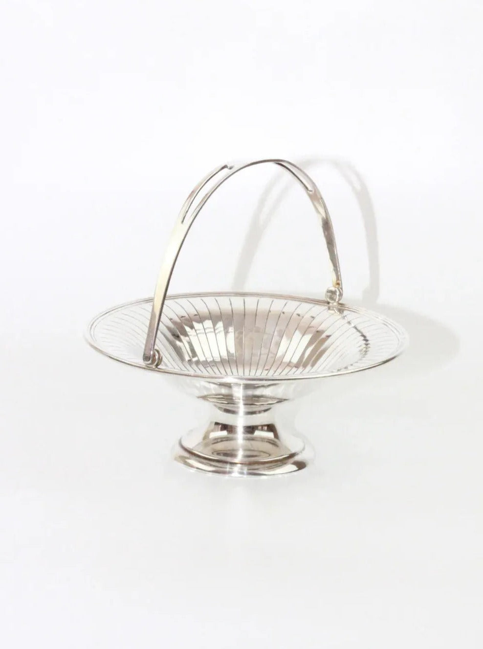 A Silver Fruit Bowl by Boga Avante Shop features a shiny nickel silver round, shallow bowl that sits on a short pedestal base. This vintage piece includes an arched handle and boasts an inner surface with vertical lines radiating outward in a decorative pattern. It is showcased against a plain white background.