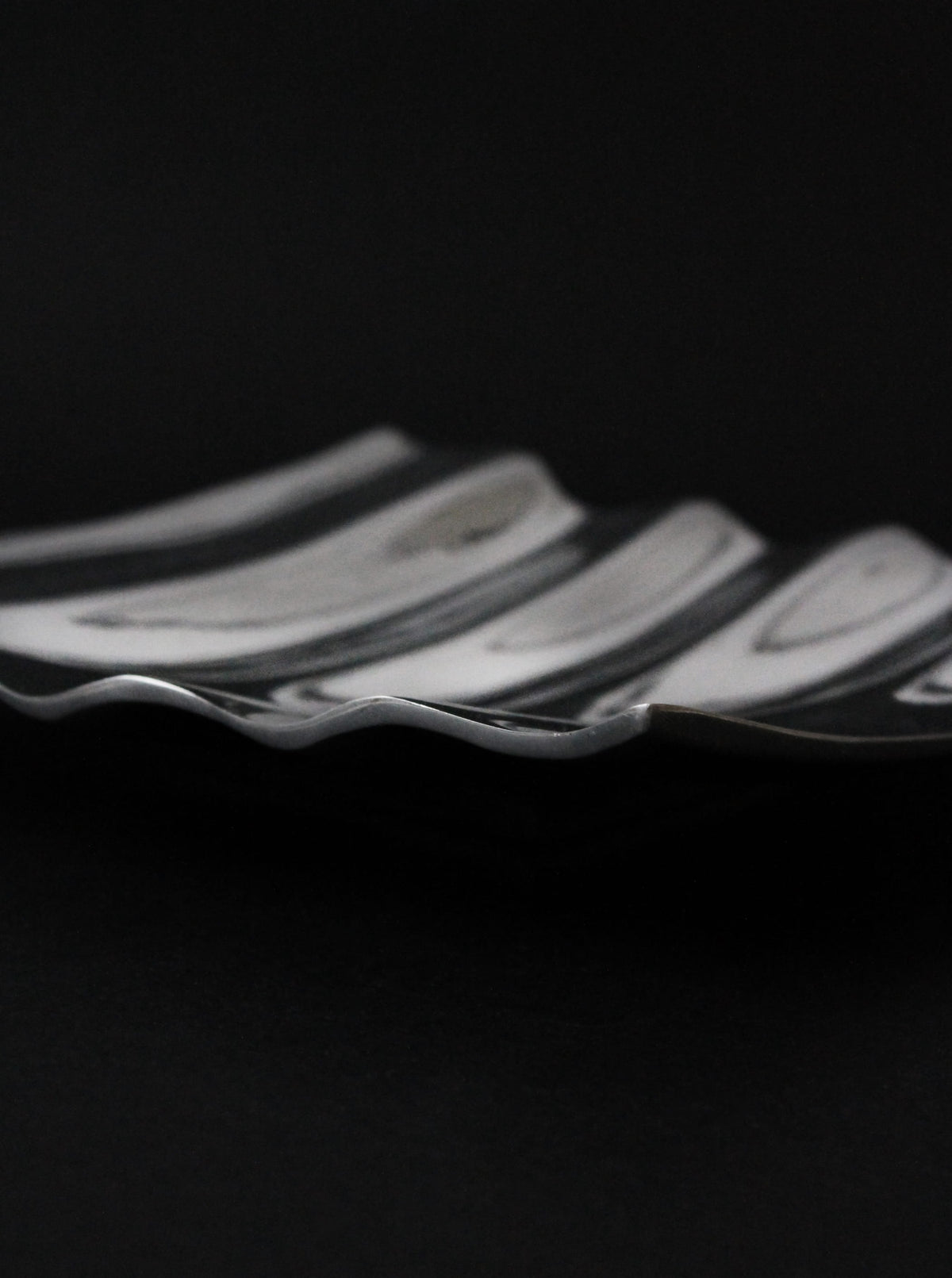 A close-up of the Vintage Stories Polished Aluminum Wave Bowl, featuring wavy edges and a sleek striped design, set against a dark background.