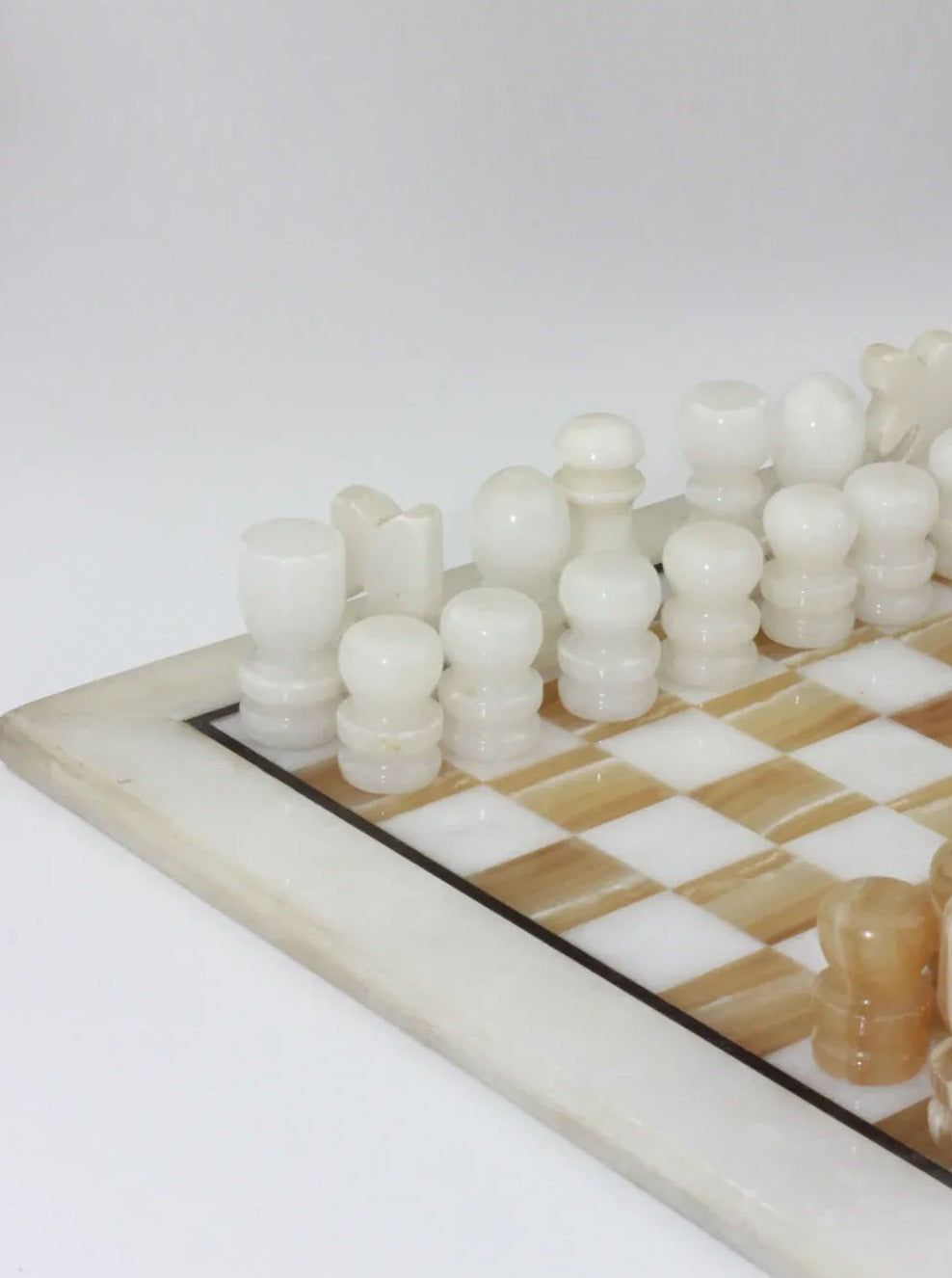 A close-up image of a Boga Avante Shop Vintage Marble Chessboard featuring neatly arranged white and beige hand-carved pieces. The board has a checkered pattern with a glossy, marble stone finish, adding a touch of elegance to the scene. The background is plain white, focusing attention on the chess setup.