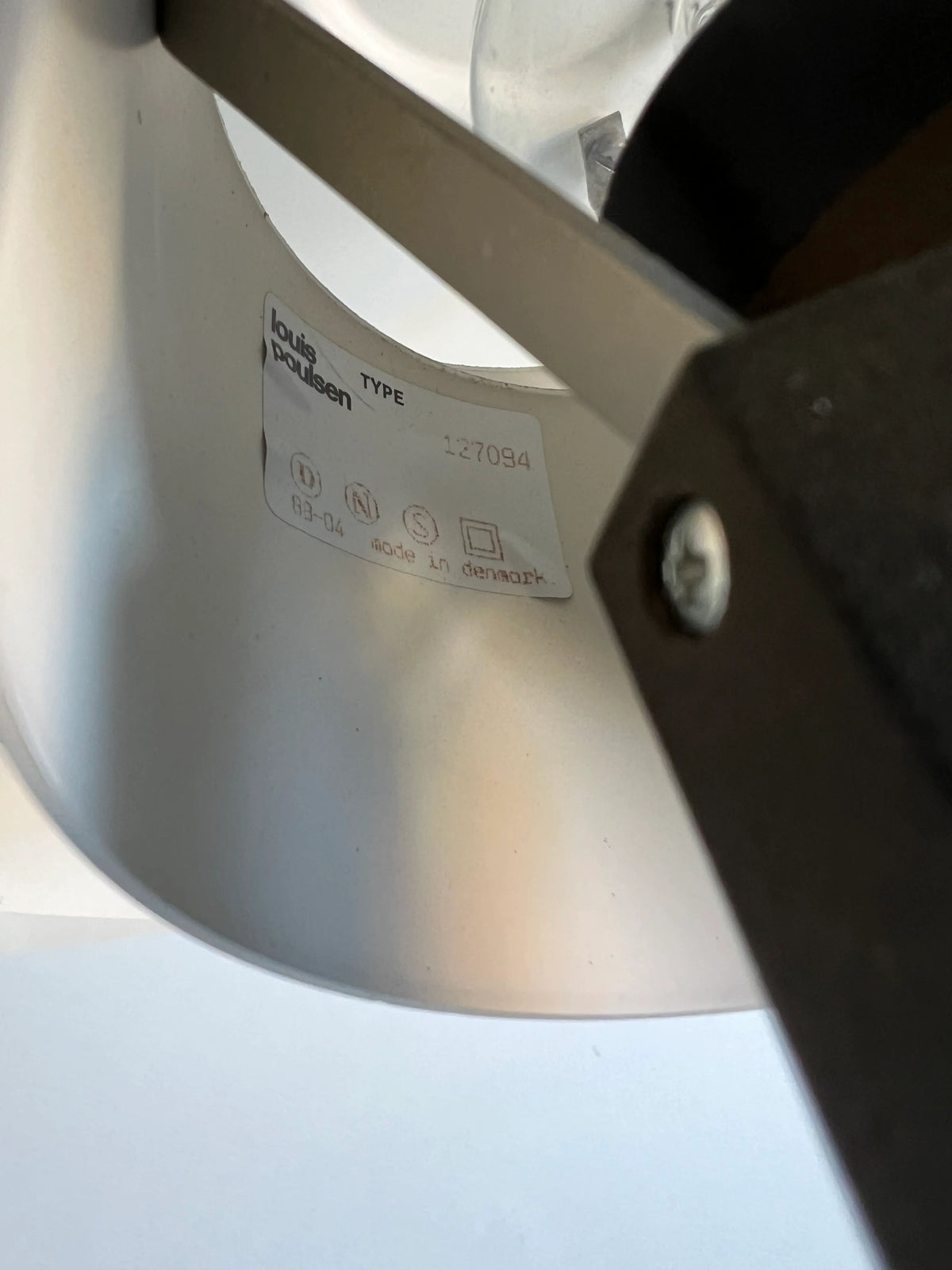 Close-up of the inside of a vintage table lamp shade showing a label with the brand name "CU-RA-TED" and text indicating the lamp type "Poulsen Table Lamp PH 4/3 1983". The label, dated 1983, also includes symbols and the text "Made in Denmark". The image focuses on the assembly details and screws.