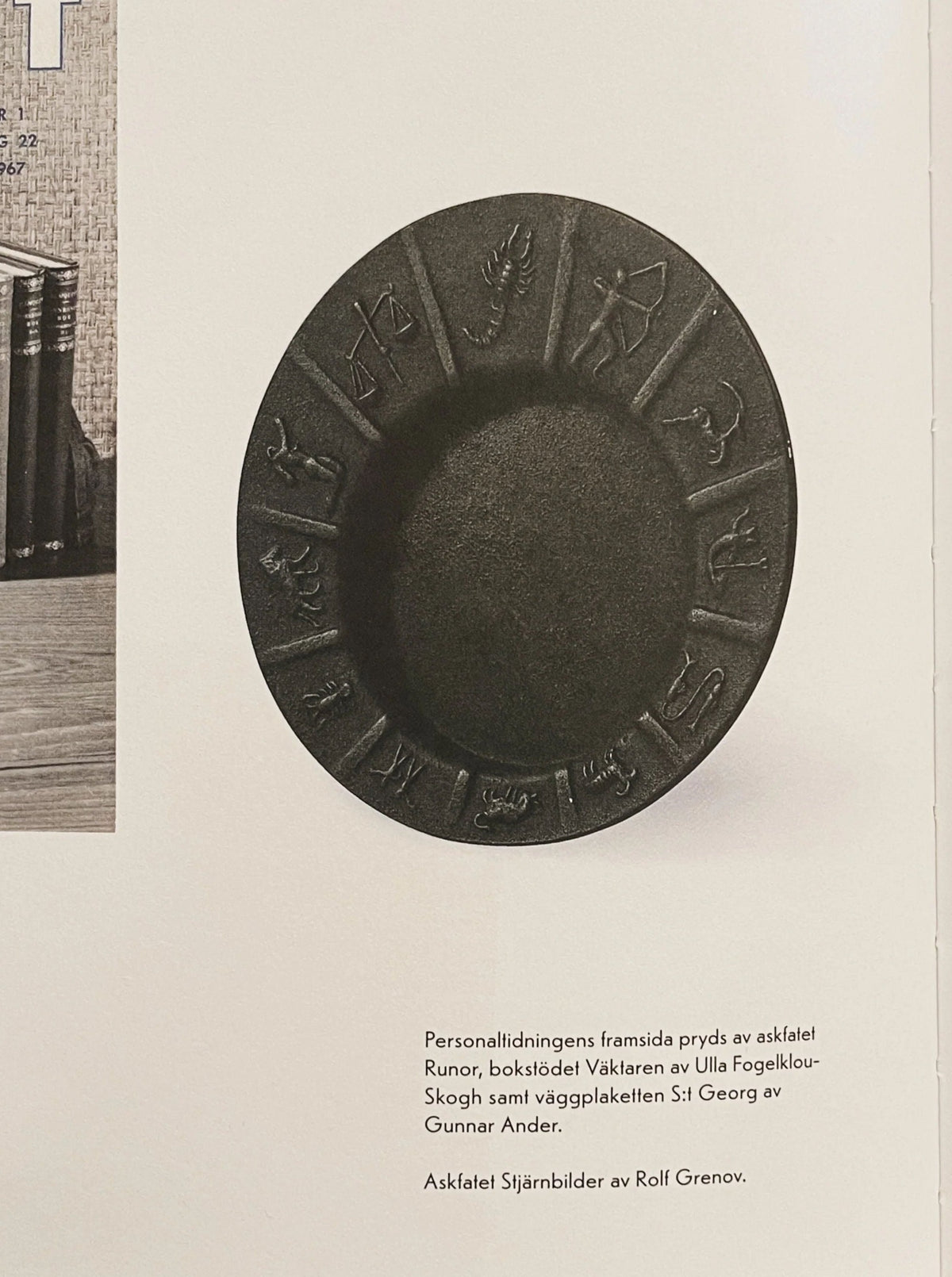 The Spigel Art Deco Zodiac Signs Decorative Dish is a round, dark-colored vintage iron dish adorned with intricate designs and etched symbols around its edge, presented against a plain background. Below the plate, some text in Swedish can be seen along with an image of a book in the upper left corner, suggesting Scandinavian vintage design influences.